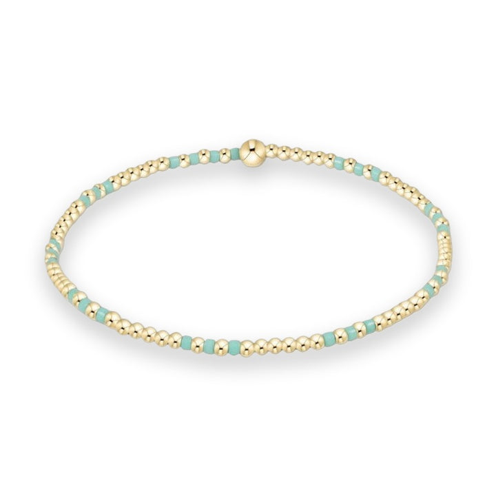 Beaded gold jewelry bracelet presented on a white background featuring small spherical gold beads and mint green cylindrical accents with a single larger central gold bead