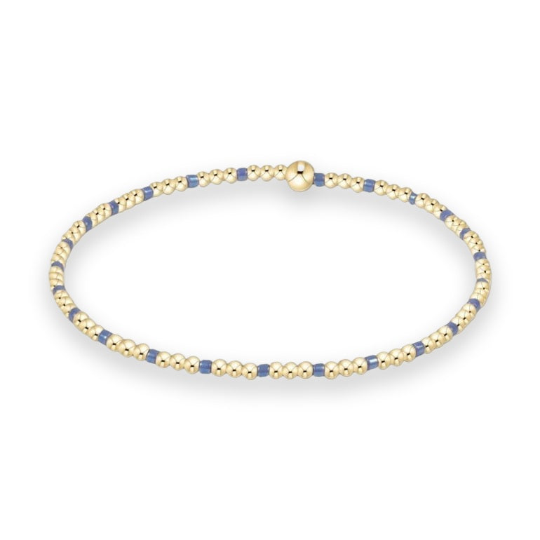 Gold beaded jewelry by Enewton featuring a stretch bracelet with an alternating pattern of three polished gold spheres and single blue cylindrical beads centered with a larger gold bead on a white background