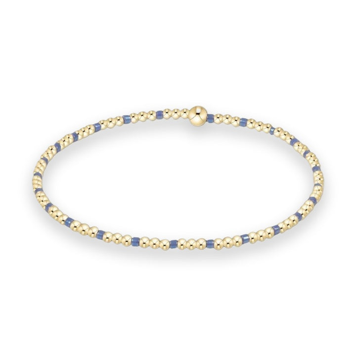Gold beaded jewelry by Enewton featuring a stretch bracelet with an alternating pattern of three polished gold spheres and single blue cylindrical beads centered with a larger gold bead on a white background