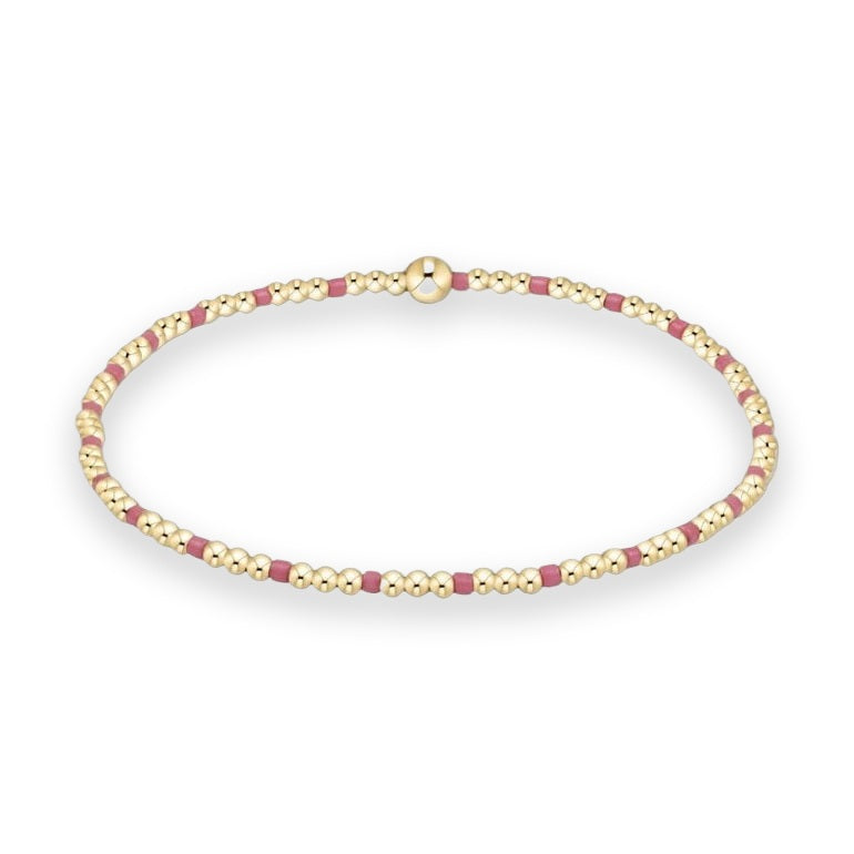 Gold-filled beaded bracelet displayed on a white studio background featuring a repeating pattern of polished yellow gold spheres, matte magenta cylindrical spacers, and a singular larger central focal bead
