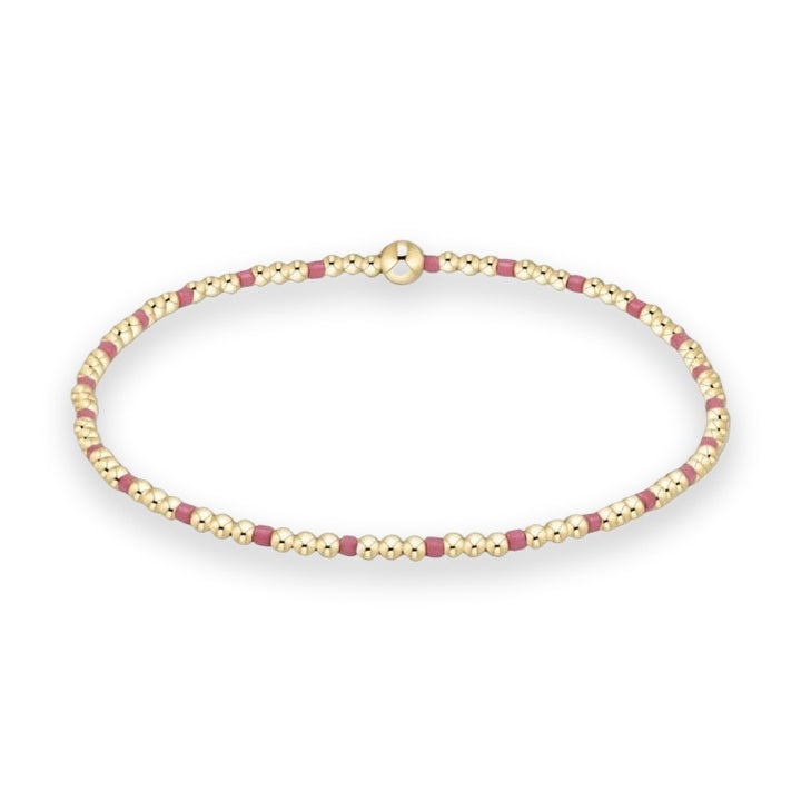 Gold-filled beaded bracelet displayed on a white studio background featuring a repeating pattern of polished yellow gold spheres, matte magenta cylindrical spacers, and a singular larger central focal bead