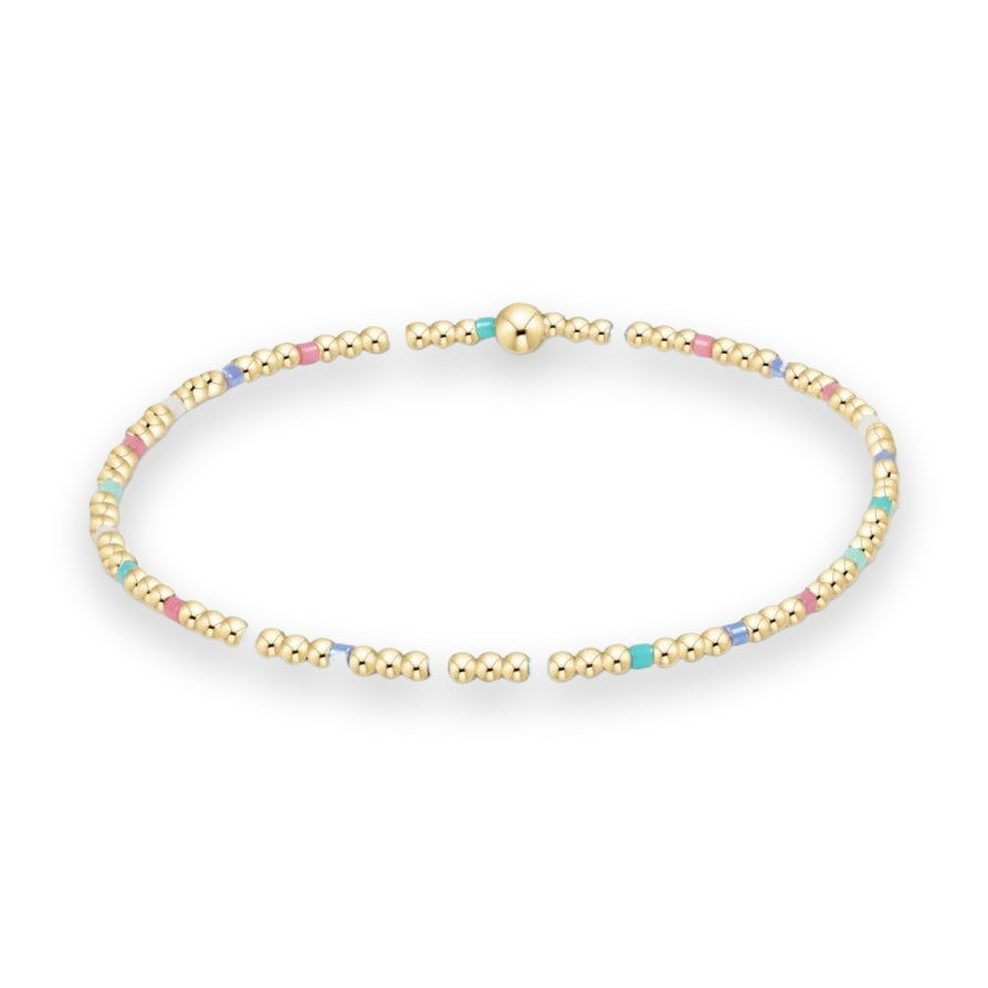 Gold-plated beaded jewelry featuring a delicate bracelet with colorful pastel pink and turquoise enamel accents and a central large polished gold bead isolated on a white background