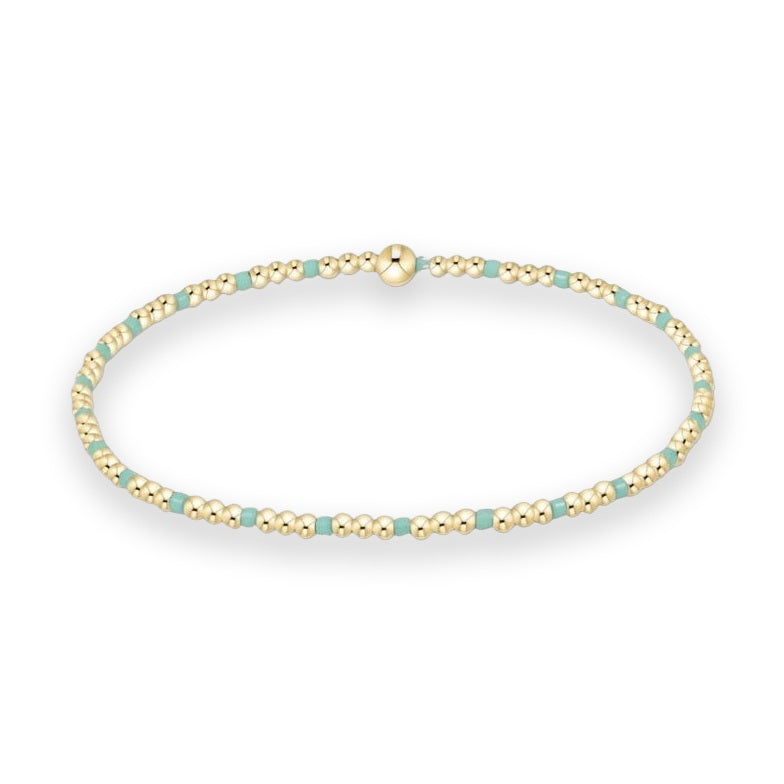 Gold-filled beaded bracelet by enewton displayed on a white studio background featuring polished spherical beads alternating with square turquoise enamel spacers and a central signature logo bead