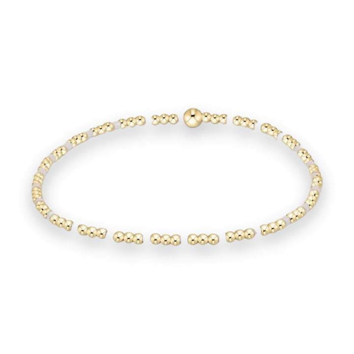 Gold-plated beaded bracelet featuring small polished spheres, cylindrical pale lavender accent beads, and a larger central focal ball bead against a white studio background