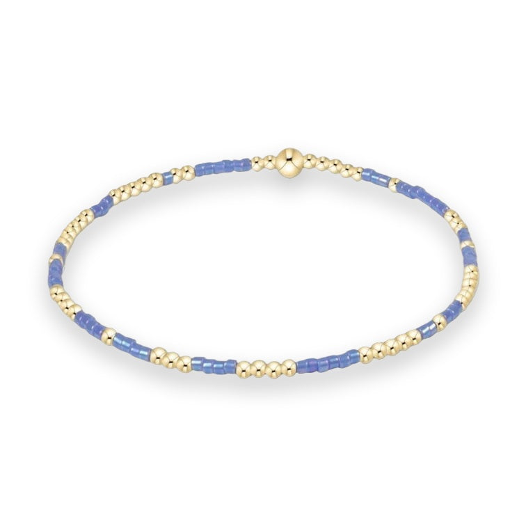 Handcrafted beaded bracelet featuring an alternating sequence of polished gold-tone spherical beads and periwinkle blue cylindrical seed beads centered with a prominent gold bead on a white background