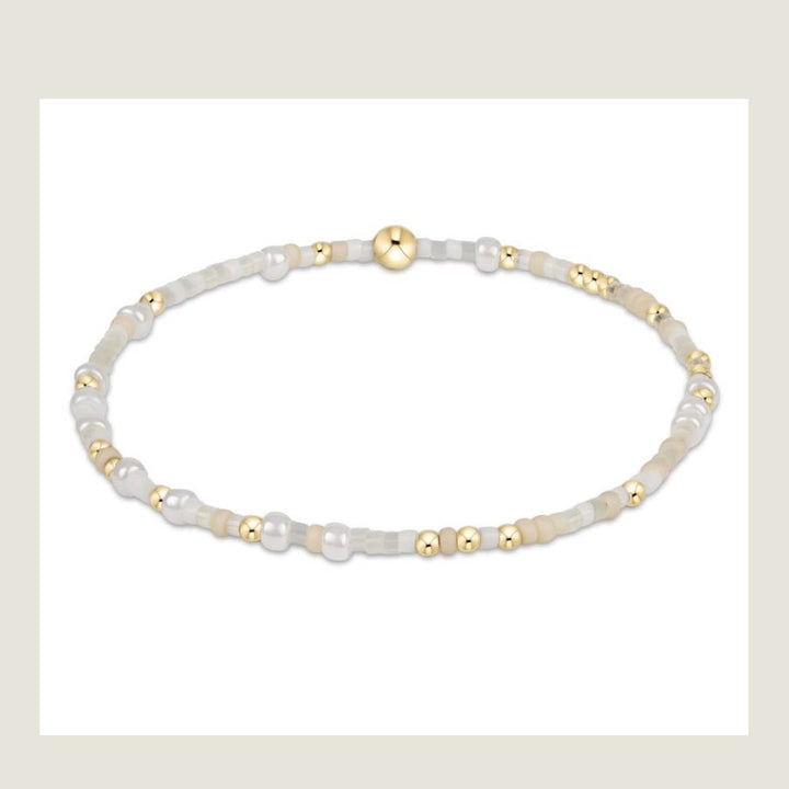Beaded jewelry bracelet centered on a white background showcasing a delicate mix of iridescent white and matte cream seed beads accented with polished gold-tone spheres and a larger central gold bead