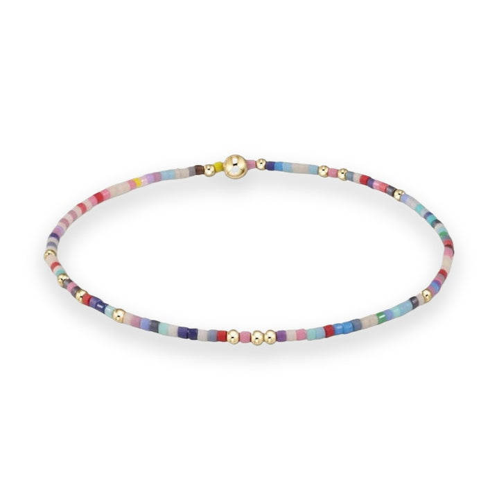 Handcrafted beaded jewelry featuring a slim multicolored bracelet on a plain white background with vibrant matte seed beads, polished gold-toned spacers, and a prominent central gold-tone sphere
