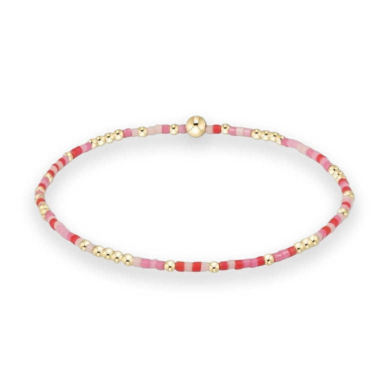 Beaded jewelry bracelet centered against a white background featuring an alternating pattern of vibrant red, soft pink, and magenta seed beads accented by small polished gold spheres and a single larger gold accent bead