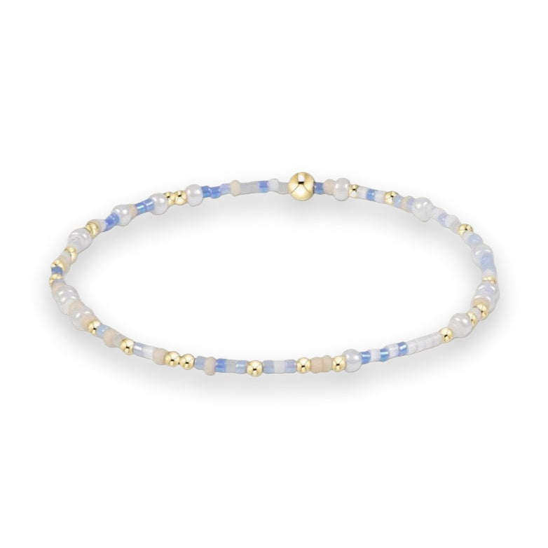 Handcrafted beaded jewelry bracelet on a white background featuring a sequence of light blue and white seed beads accented with polished gold-tone spheres and a central larger gold bead