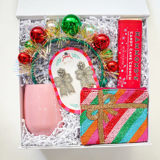 Gift box with pink stemless wine glass, decorative wreath, and colorful striped gift box on a white background