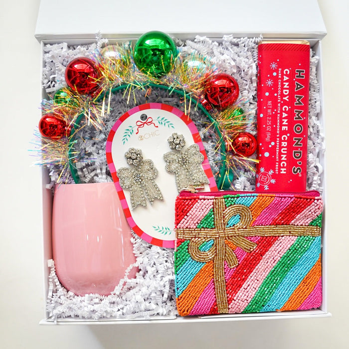 Gift box with pink stemless wine glass, decorative wreath, and colorful striped gift box on a white background