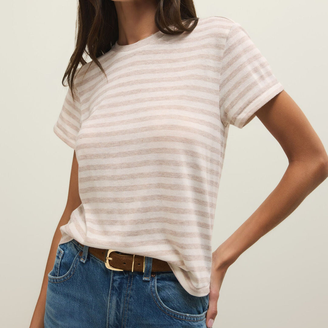 Fashion photograph of a woman in a studio setting wearing a beige and white horizontally striped t-shirt tucked into blue denim jeans featuring a brown suede belt with a gold buckle
