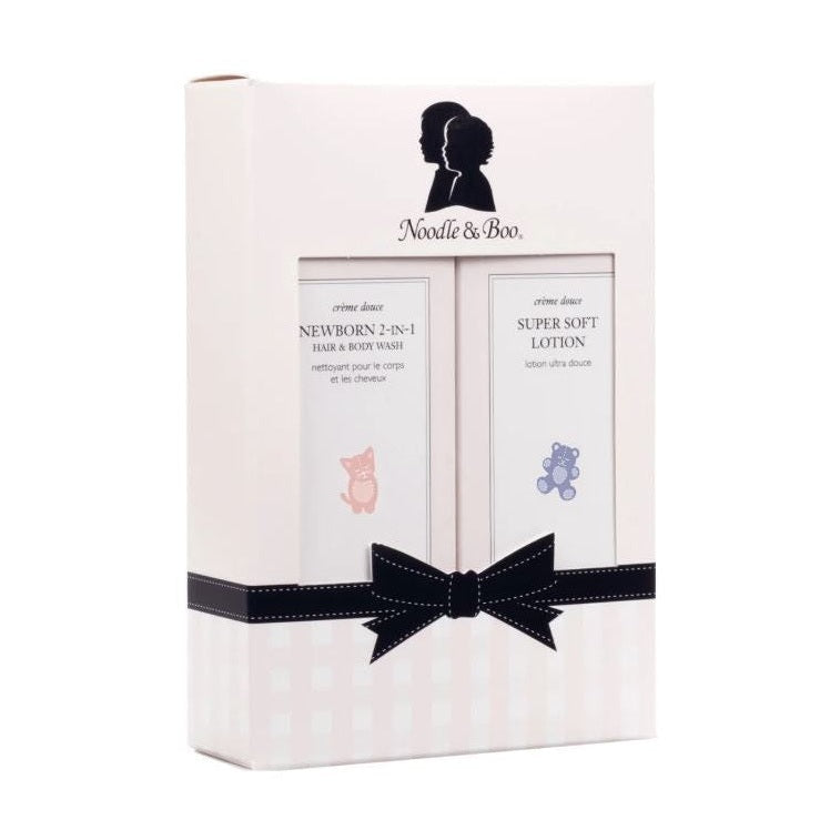 Product photograph by Noodle & Boo featuring a white gift set box for newborn wash and lotion with a black mother and child silhouette logo, a pink kitten and purple teddy bear illustration, and a black bow with white stitching