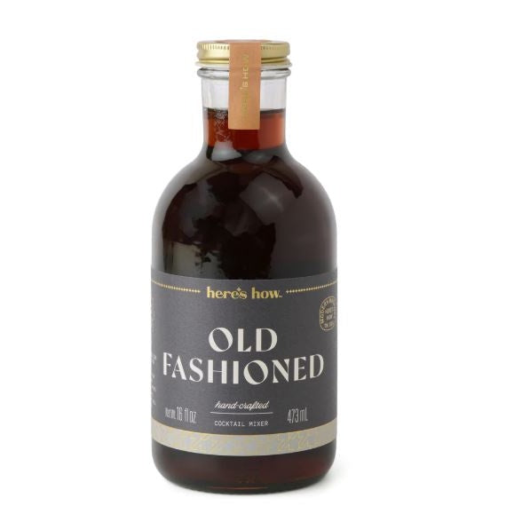 Product photograph of a here's how. Old Fashioned cocktail mixer bottle on a white background featuring a charcoal gray label with gold lettering, rich dark amber liquid, and a metallic gold cap