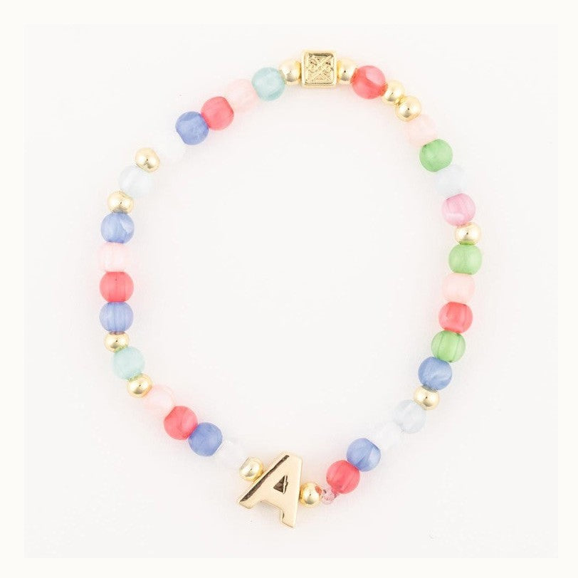 Handcrafted beaded jewelry piece featuring a colorful initial bracelet on a white background with a gold-tone letter A charm, multi-colored cat-eye beads, and a square metal logo bead