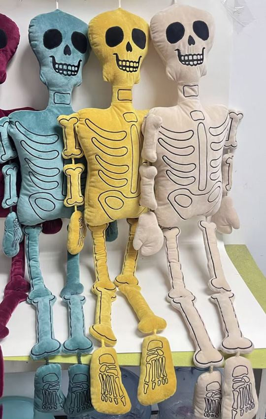 Three plush skeletons in blue, yellow and cream hanging side by side