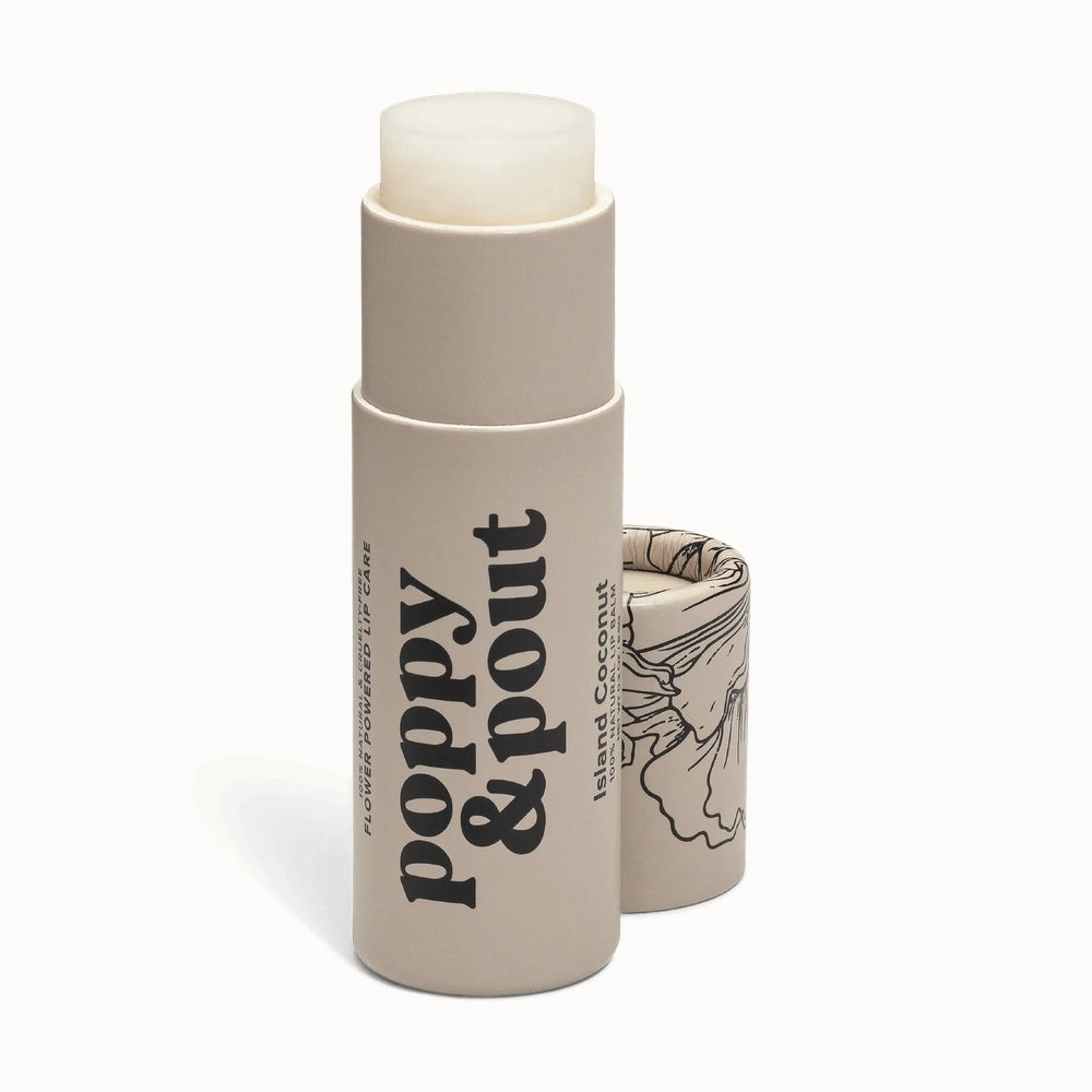 Product photograph by Poppy & Pout of an Island Coconut lip balm tube on a black background featuring a tan cardboard container with bold black serif typography and an intricate floral line drawing on the cap
