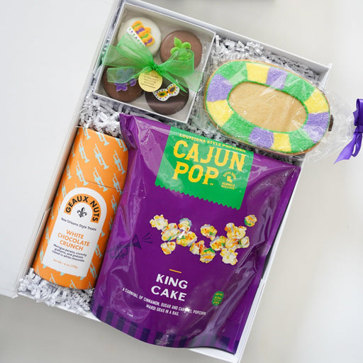 Gift set with cookies, King Cake popcorn, and a bottle of orange juice in a white box with a green ribbon.