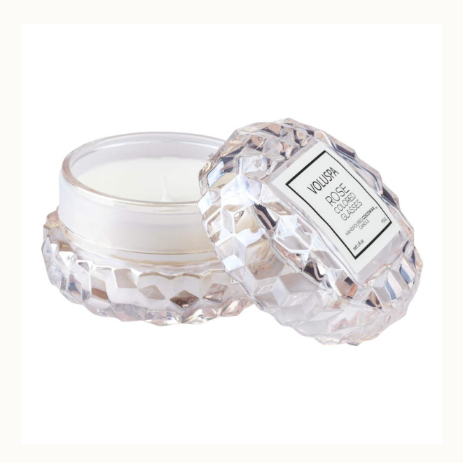 Product photography of a Voluspa Rose Colored Glasses scented candle featuring a faceted geometric glass jar and lid with a white square brand label and smooth white hand-poured coconut wax against a plain white background