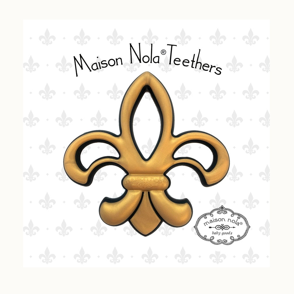 Silicone baby teether designed by Maison Nola featuring the iconic New Orleans fleur-de-lis symbol in a matte gold finish with black trim and embossed center logo against a white patterned backdrop