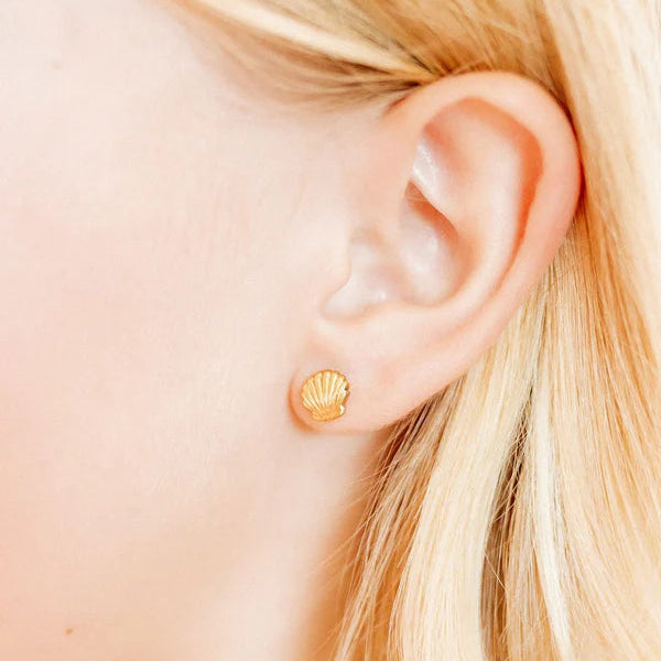 Digital photograph of a gold scallop shell stud earring worn on a woman's earlobe featuring textured radial ridges and a polished finish against soft blonde hair
