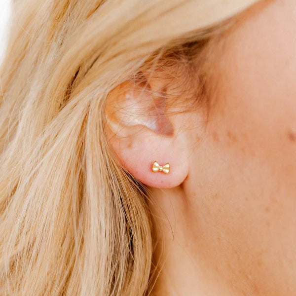 Digital photograph of a dainty yellow gold bow stud earring worn on a woman&