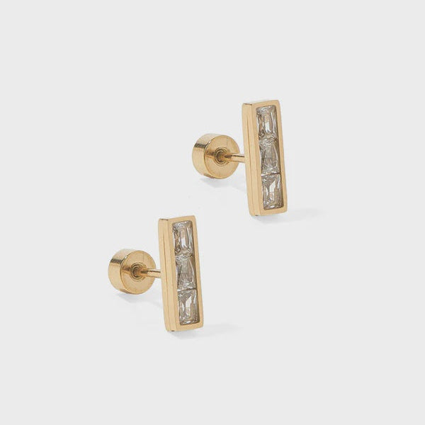 Gold jewelry featuring a pair of bar stud earrings with three clear baguette-cut stones in a vertical channel setting and secure screw-back posts on a light gray background