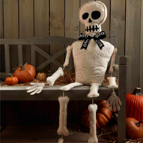 Stuffed fabric skeleton sitting on a wooden bench with pumpkins