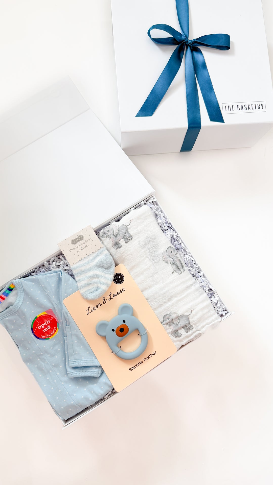 Baby gift set with clothes, blanket, and teether on a white surface