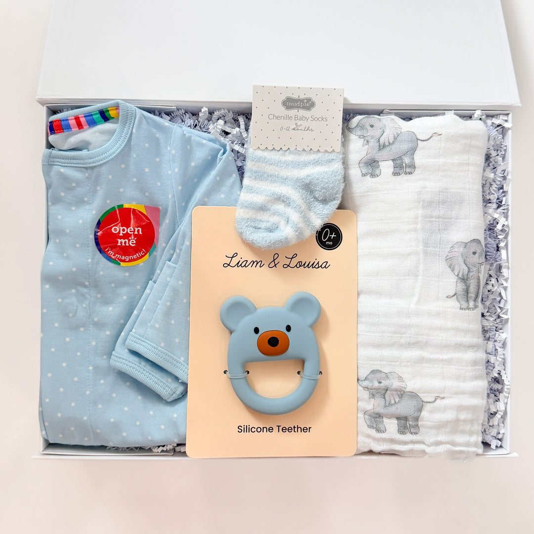 Baby product set with blue clothing, teether, and bibs in a box on a white background