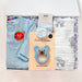 Baby product set with blue clothing, teether, and bibs in a box on a white background