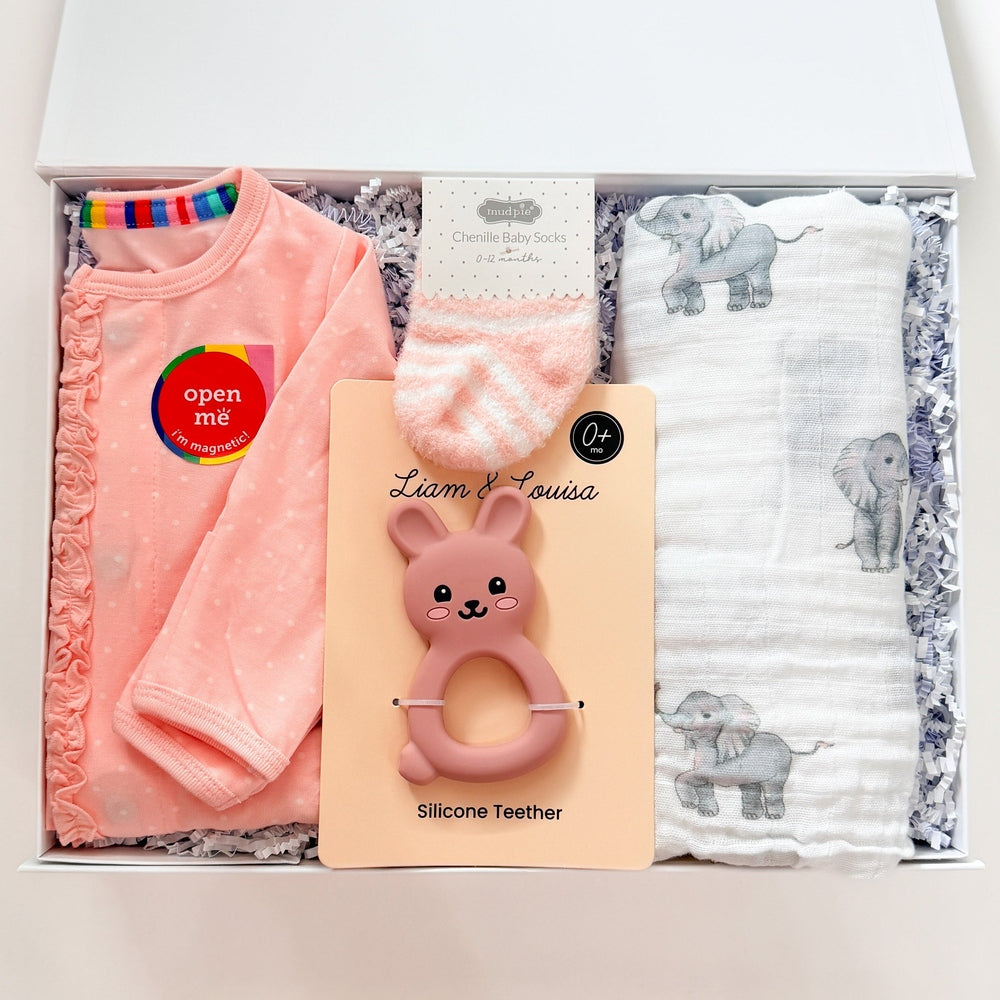 Baby gift set with pink baby clothes, teether, and blanket in a box on a white background