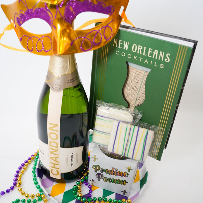 Bottle of champagne, Mardi Gras mask, beads, and New Orleans cocktail book on a white background