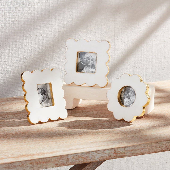 Three small white scalloped frames with gold edges on a wooden table
