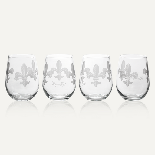 Glassware by Mignon Faget features four stemless wine glasses with frosted fleur-de-lis icons of New Orleans on a reflective neutral background highlighting delicate diagonal line textures and a script signature logo