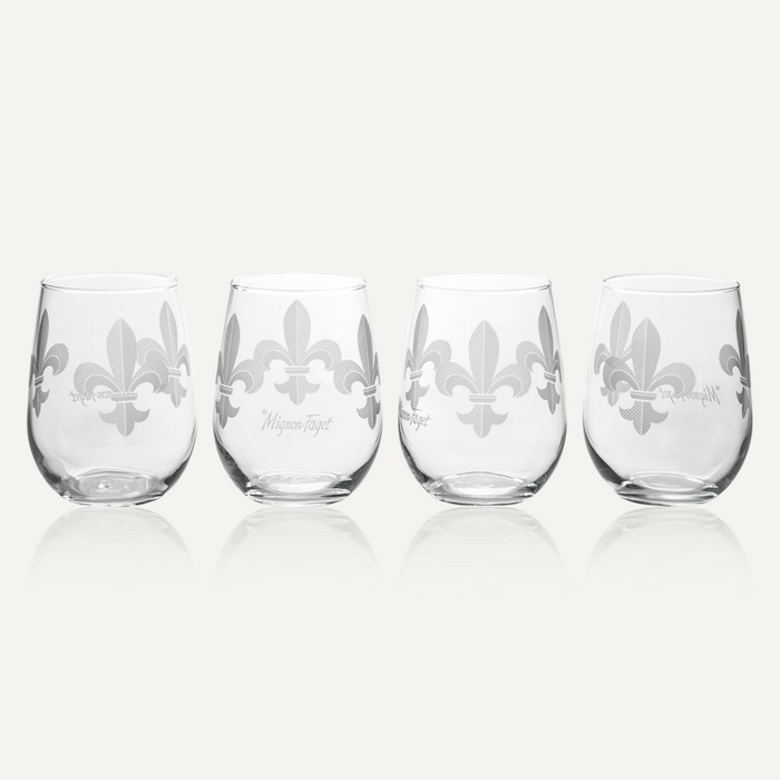 Glassware by Mignon Faget features four stemless wine glasses with frosted fleur-de-lis icons of New Orleans on a reflective neutral background highlighting delicate diagonal line textures and a script signature logo