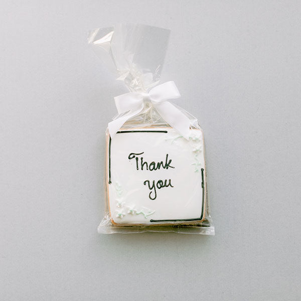 Square sugar cookie iced white with Thank You in script, wrapped in cellophane with a white bow