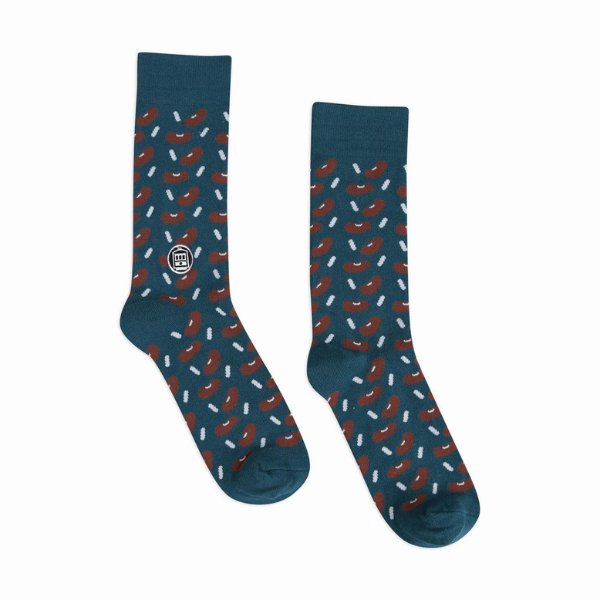 Woven cotton blend socks by Bonfolk Collective featuring a New Orleans-themed red beans and rice pattern with an iconic St. Charles streetcar logo, scattered brown kidney beans, and textured white rice grains on a deep teal background