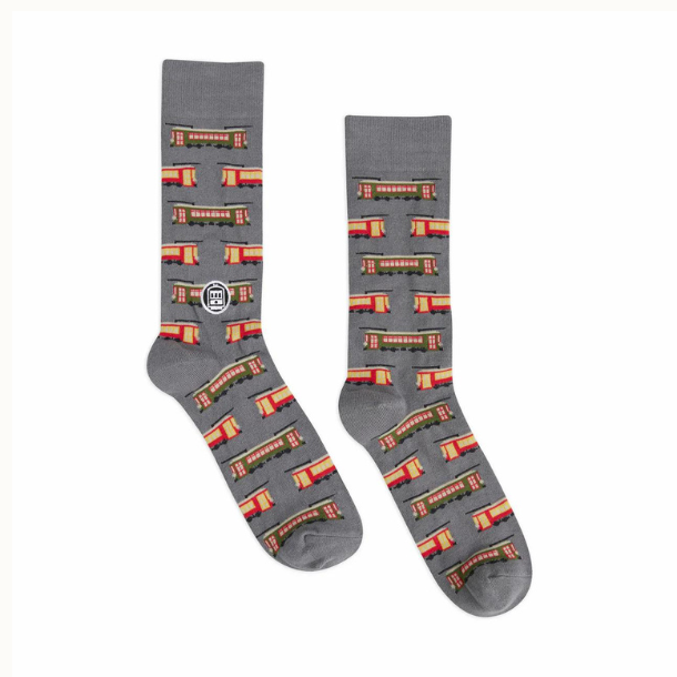 Textile crew socks by Bonfolk showcasing a repeating pattern of iconic New Orleans streetcars including the green St. Charles and red Canal Street lines set against a grey background with detailed yellow window accents
