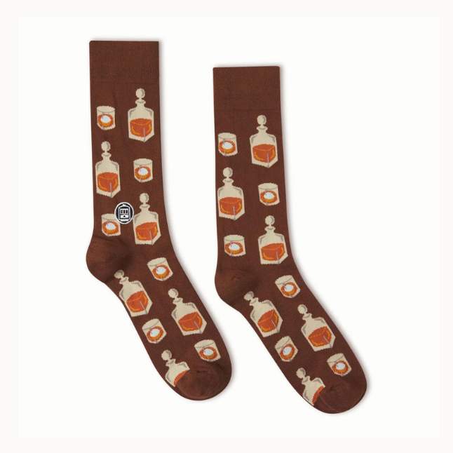Knitted cotton socks by Bonfolk featuring a chocolate brown background patterned with amber-filled whiskey decanters and ice-filled tumblers alongside a white New Orleans streetcar logo