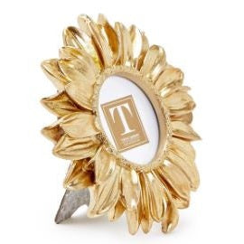 Decorative gold-toned metal frame by Tess Taylor Collection featuring a sunflower-shaped subject on a white background with layered metallic petals, a circular photo aperture, and a gray easel stand