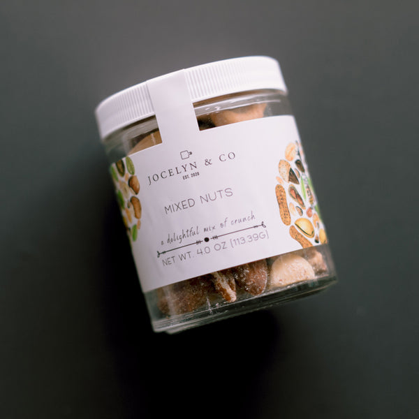 Clear jar of Jocelyn &amp; Co mixed nuts with a white lid on a dark background
