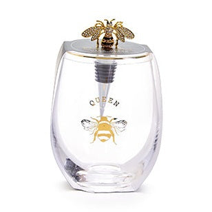 Decorative glassware by The Queens' Jewels featuring a clear stemless wine glass and bejeweled stopper on a white background with a gold queen bee emblem and sparkling rhinestone-encrusted wings