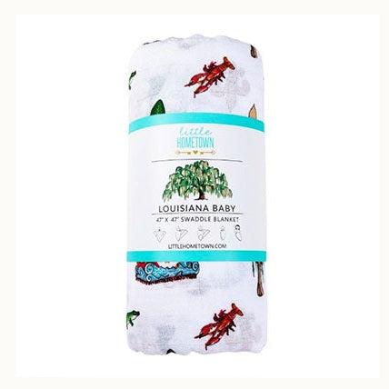 Watercolor illustration by Little Hometown of a Louisiana-themed baby swaddle blanket featuring iconic regional symbols including a vibrant red crawfish, a lush green live oak tree, and a colorful festive parade float on white muslin fabric