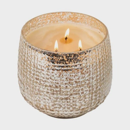 Studio photograph of a three-wick scented candle in a textured champagne mercury glass jar on a neutral background featuring three flickering orange flames and a shimmering metallic hobnail finish