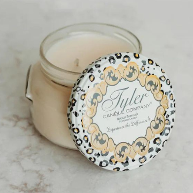Photograph of a Tyler Candle Company jar candle on a light marble surface featuring a decorative lid with a leopard print border, gold ornate flourishes, and smooth ivory-colored wax