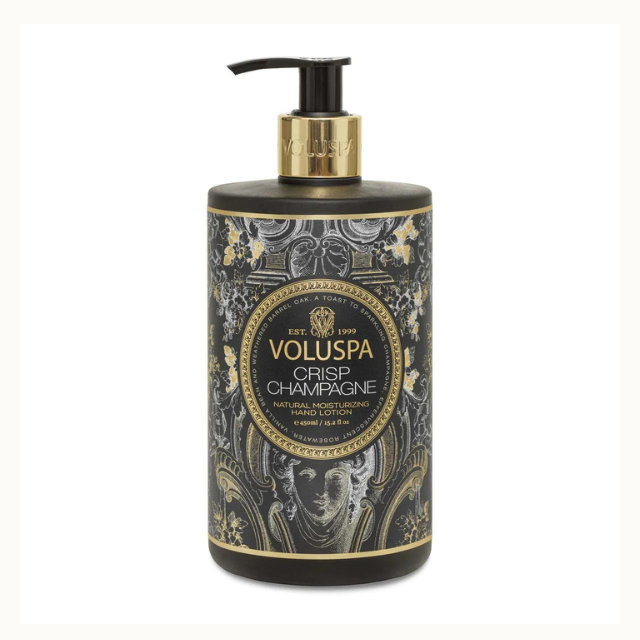 Product photography for Voluspa featuring a bottle of Crisp Champagne natural moisturizing hand lotion centered on a white background with an intricate black and gold damask label and a classical portrait illustration beneath a gold pump collar
