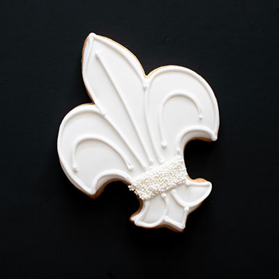 White-iced fleur-de-lis sugar cookie with pearl sprinkles on a black background