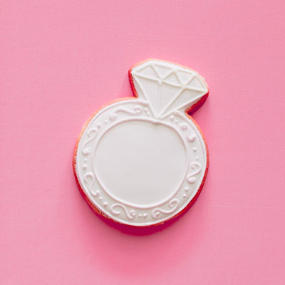 Sugar cookie iced white in the shape of a diamond ring on a pink background