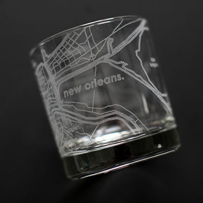 Etched glass rocks glass featuring a detailed map of New Orleans including the winding Mississippi River and French Quarter street grid rendered in frosted white lines with lowercase typography and a heavy weighted base
